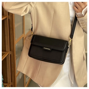 Détail du sac bandoulière en cuir noir avec logo doré et attaches métalliques dorées