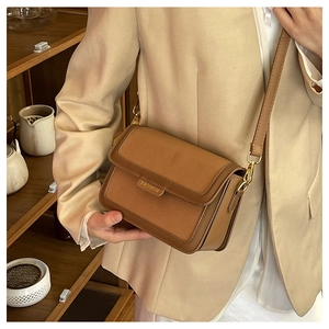 Détail d'un sac bandoulière marron avec emblème doré FASHION et texture de cuir