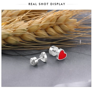 Macro shot of silver heart stud earrings with red enamel and natural wheat decor