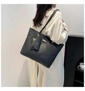 Détail d'un grand sac cabas noir en cuir grainé avec petite pochette porté par un mannequin
