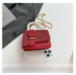 Mini sac rouge à paillettes avec anse en perles et chaîne à côté d'un smartphone