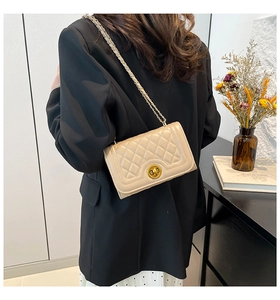 Detailed view of beige quilted handbag featuring a golden circular twist lock and chain strap