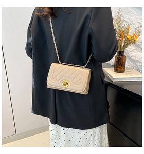 Quilted beige shoulder bag with gold chain strap and metal lock shown on a model
