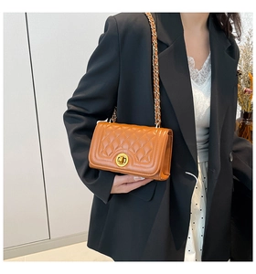 Detail of brown quilted chain bag with gold rotary clasp on a model in a black blazer
