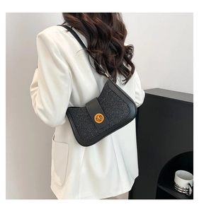 Detail of a chic black shoulder bag with shimmering texture and golden circular buckle