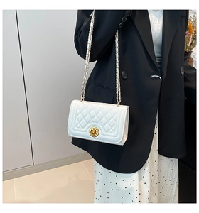 Detail of white quilted handbag with golden chain strap and twist lock on a black suit