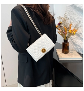 Close-up of white quilted crossbody bag with gold chain strap worn by a model in black suit