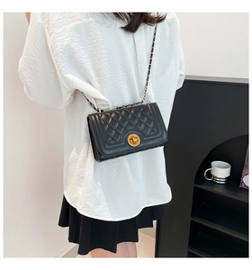 Detail of black quilted leather shoulder bag with gold clasp and chain strap on model
