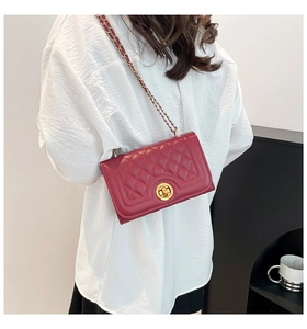 Macro view of burgundy quilted shoulder bag with gold chain strap and turn-lock closure