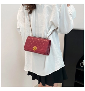 Detail view of burgundy quilted crossbody bag with gold lock and chain strap on shoulder