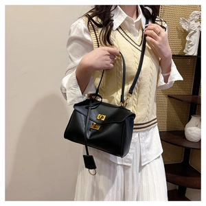 Detail of minimalist black leather shoulder bag with gold metal twist locks and charm