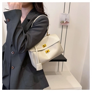 Detail of cream white leather handbag with dual gold twist locks on a grey blazer