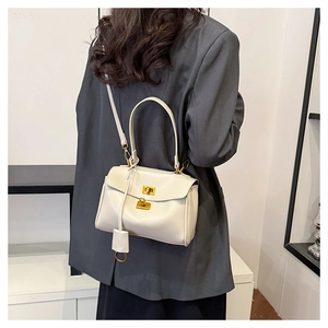 Detail of a creamy white leather handbag with a gold square twist lock on a grey blazer