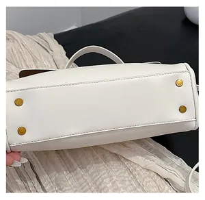 Close-up of white leather handbag base featuring four golden metal feet and precise stitching