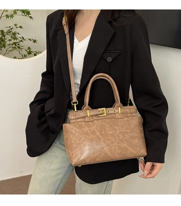 Brown vintage leather tote bag with gold buckle detail and adjustable strap held by model