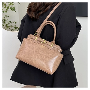 Close-up of vintage tan crossbody bag with gold buckle on a model in a black suit
