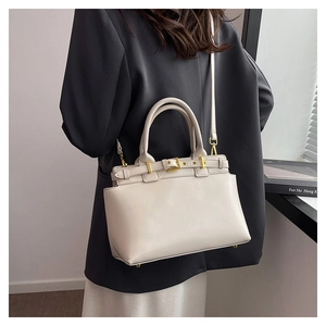 Detail of cream leather tote bag with gold hardware and protective base feet on a model