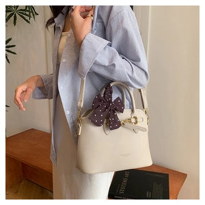 Detail of cream leather tote bag featuring a brown polka dot ribbon and gold hardware