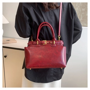 Close-up of burgundy retro tote bag with glossy faux leather texture and golden buckles