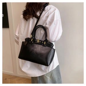 Detail of glossy black tote bag with gold metal buckles and crossbody strap on a model
