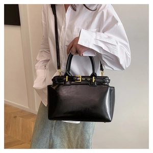 Detail of black faux leather tote bag with gold buckle strap and polished finish