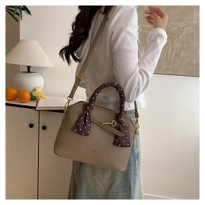 Close-up of brown litchi pattern leather tote bag with decorative polka dot silk scarf handle