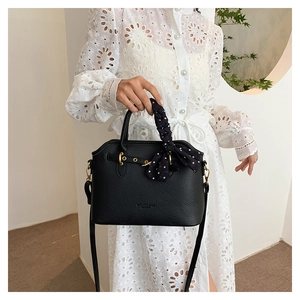 Detail of black litchi grain tote bag with gold hardware and polka dot silk scarf handle