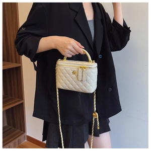 Detail of white quilted bucket bag featuring a gold floral emblem and metal chain strap