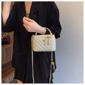 Detail of white quilted box bag featuring a gold floral clasp and chain strap on a black blazer