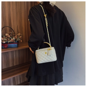 Detailed view of white quilted leather box bag with gold chain strap on shoulder