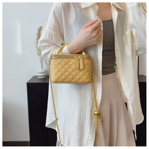 Detail of light yellow quilted box bag featuring camellia logo and adjustable chain strap