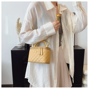 Close-up of yellow quilted chain bag with camellia detail and gold metal handle