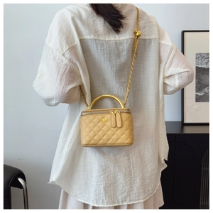 Crossbody view of a beige quilted vanity case bag with gold flower logo and chain strap