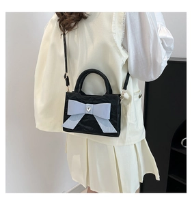 Detail view of glossy black pleated bag with a large light blue bow and heart rhinestone