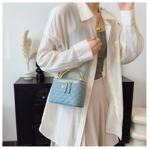 Macro shot of light blue quilted bag with gold metal handle and chain shoulder strap