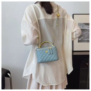 Rear view of a model wearing a light blue quilted mini box bag with gold chain strap