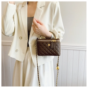 Detail view of coffee quilted box bag featuring golden camellia charm and chain strap