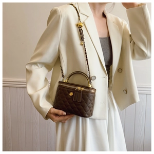 Close-up of quilted brown box bag with golden metal handle and camellia charm detail