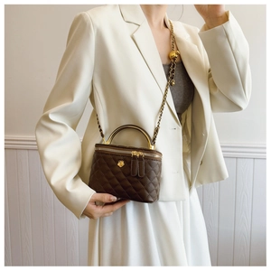 Detail of dark brown quilted box bag with golden camellia logo and metal chain strap