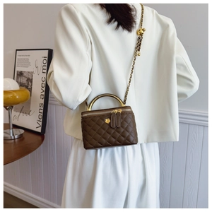 Detail of dark brown quilted box bag with gold floral clasp and chain strap on a model
