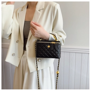 Detail of black quilted leather vanity bag with gold camellia logo and chain handle