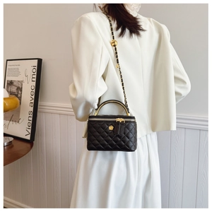 Close-up of black quilted box bag with gold metal handle and chain strap on a model
