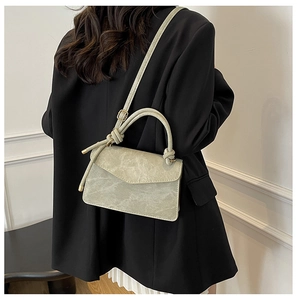 Detailed back view of a light green crossbody bag with a knot handle on a black suit