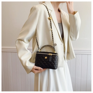 Detail of black quilted crossbody bag with gold handle on white suit outfit
