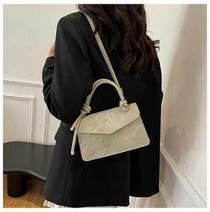 Detail of sage green envelope crossbody bag with knot handle worn over a dark blazer