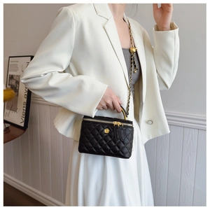 Detail of black quilted leather vanity bag with gold flower accent and chain strap