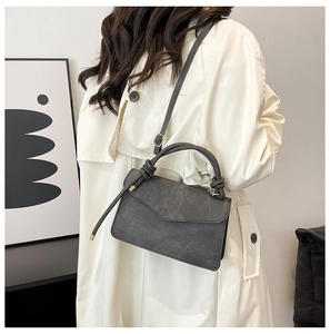 Detail of knot handle and matte texture on dark grey crossbody bag worn with trench coat