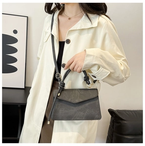 Detail of dark grey crossbody bag with cylindrical handle and fine suede texture on a model