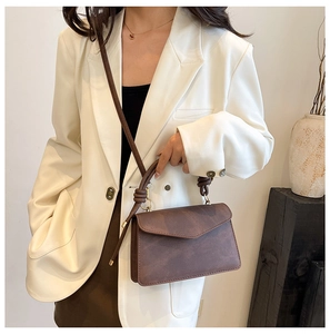 Detail view of brown matte leather handbag with unique knotted handle and V-shaped flap