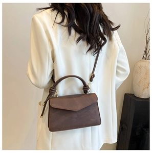 Modern dark brown crossbody bag with unique knot handle shown on a model against white walls